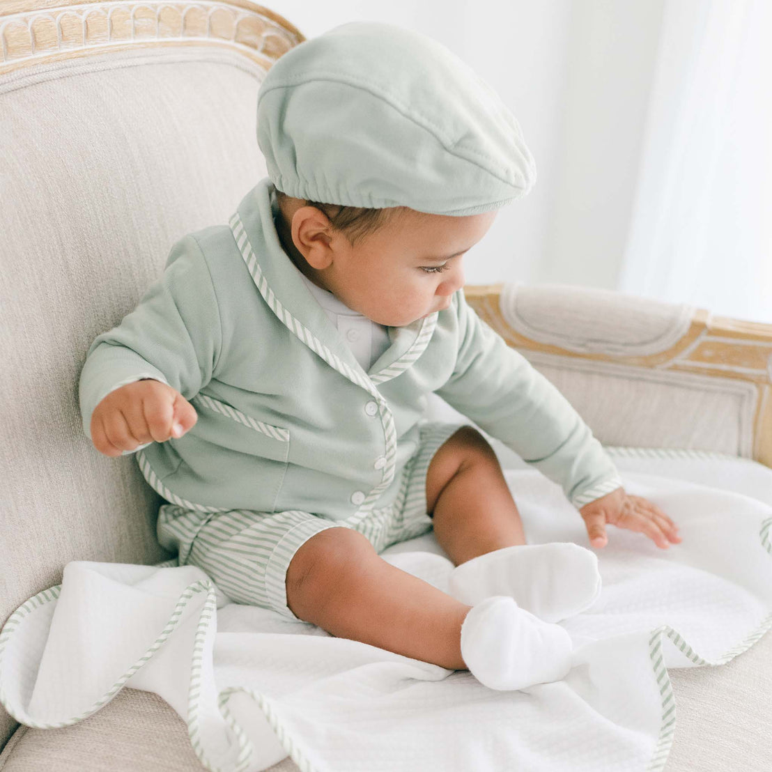Baby boy wearing the green Theodore Short Suit, including the jacket, shorts, and onesie (and matching Theodore Newsboy Cap).