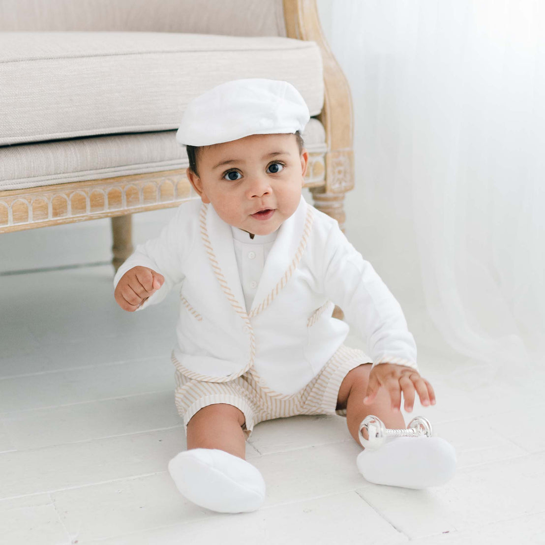 Baby boy wearing the tan Theodore Short Suit, including the jacket, shorts, and onesie (and matching Theodore Newsboy Cap).