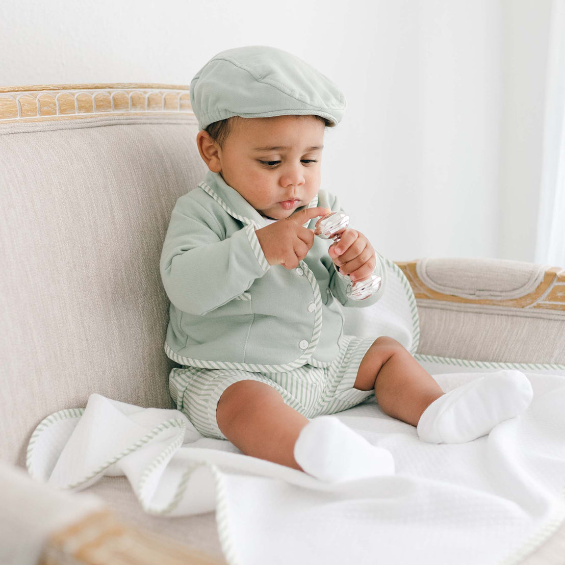 Baby boy wearing the green Theodore Short Suit, including the jacket, shorts, and onesie (and matching Theodore Newsboy Cap).