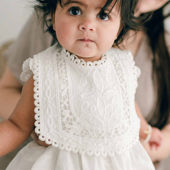 Baby wearing the Lily Lace Bib that is made out of cotton lace in light ivory and exhibits a unique squared design and circle lace trim.
