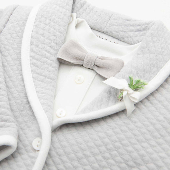 Close-up of a baby outfit, featuring a white collared shirt with a decorative Asher Grey Bow Tie & Boutonniere and buttons, overlaid by a soft textured gray cardigan.