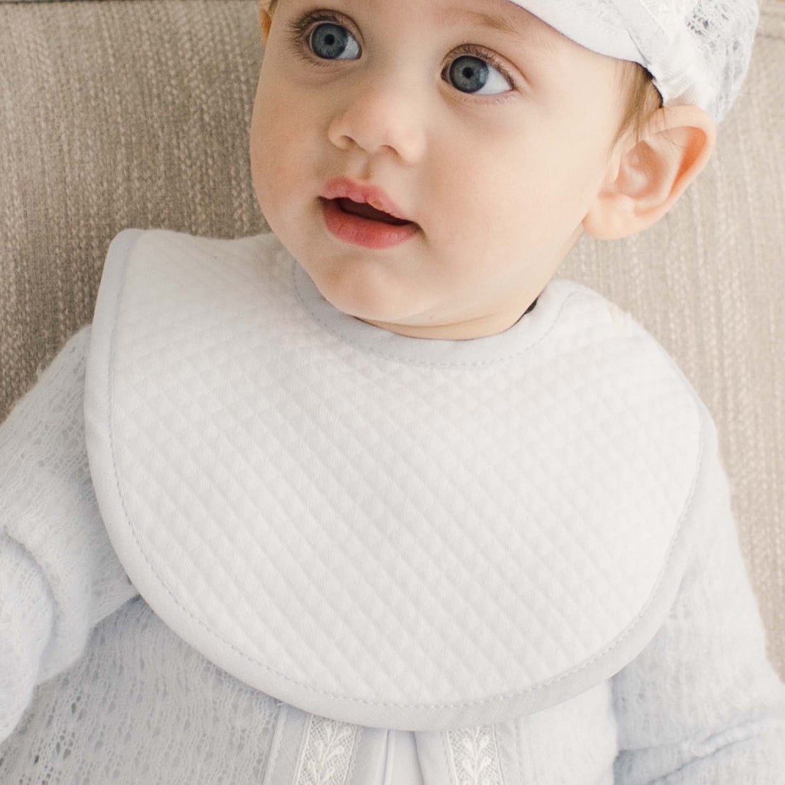 Baby wearing the Harrison white bib with blue linen trim and hat with a neutral background