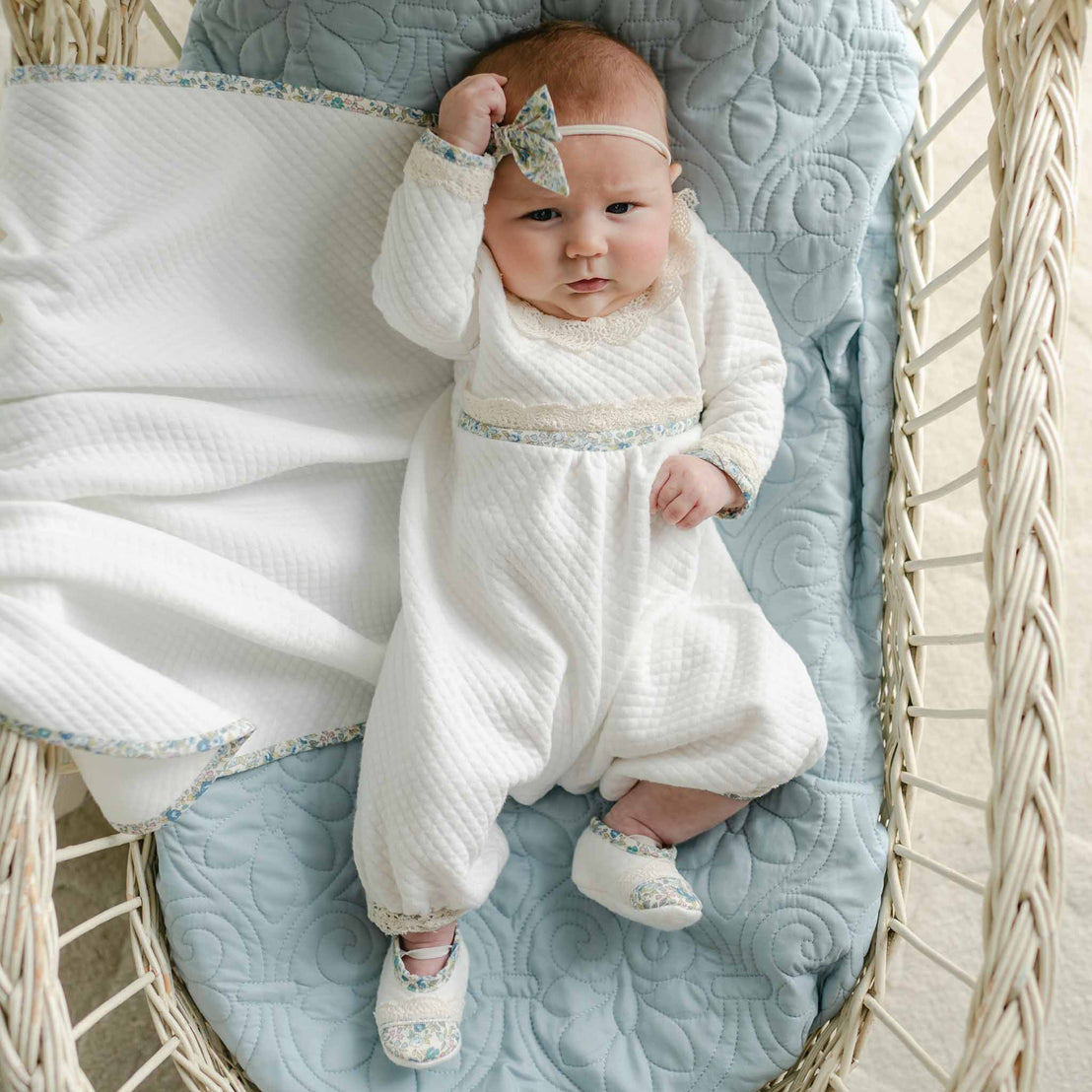 Baby lying in a basket wearing the Petite Fleur Blue Romper with matching shoes and floral bow headband.