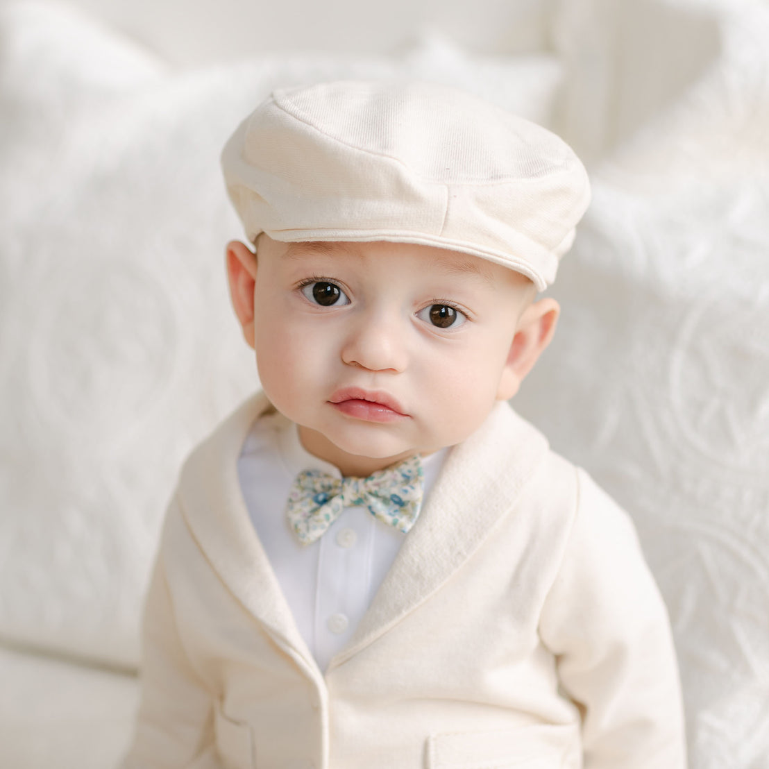 Baby wearing the Petite Fleur Blue Bow Tie and ivory cap with matching jacket.