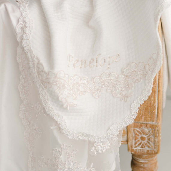 Baby girl baptism blanket draped around a chair. The name Penelope is embroidered in silk lace. 