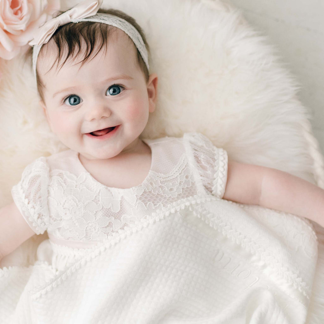 Baby girl laughing wearing the Victoria cotton layette gown, snuggled in the personalized Victoria christening blanket made of quilted cotton.