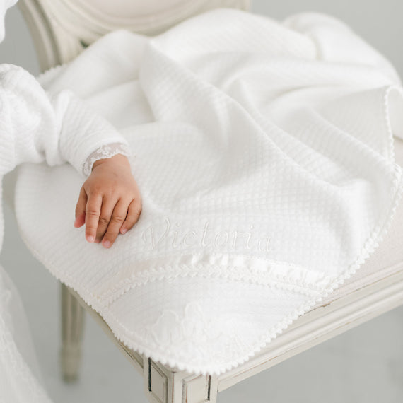 Alternative photo of the Victoria personalized baptism blanket on chair. Baby girls hand resting on corner. 