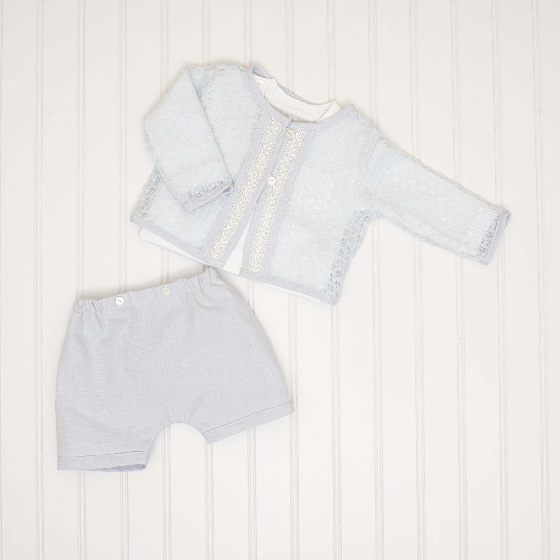 A flat lay of the Harrison Sweater 3-Piece Shorts Suit, featuring the light blue knit sweater with lace trim, coordinating shorts, and a matching onesie.