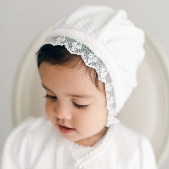 Baby girl wearing a quilted baby bonnet made of lace and cotton. Part of the Baby Beau & Belle Victoria Collection.