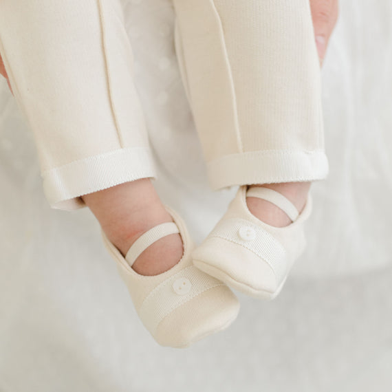 Baby wearing the Ezra Booties crafted with a super soft natural ivory French terry. It features ivory grosgrain ribbon detailing across the toe with a button finish. Soft elastic bands help keep the booties fit