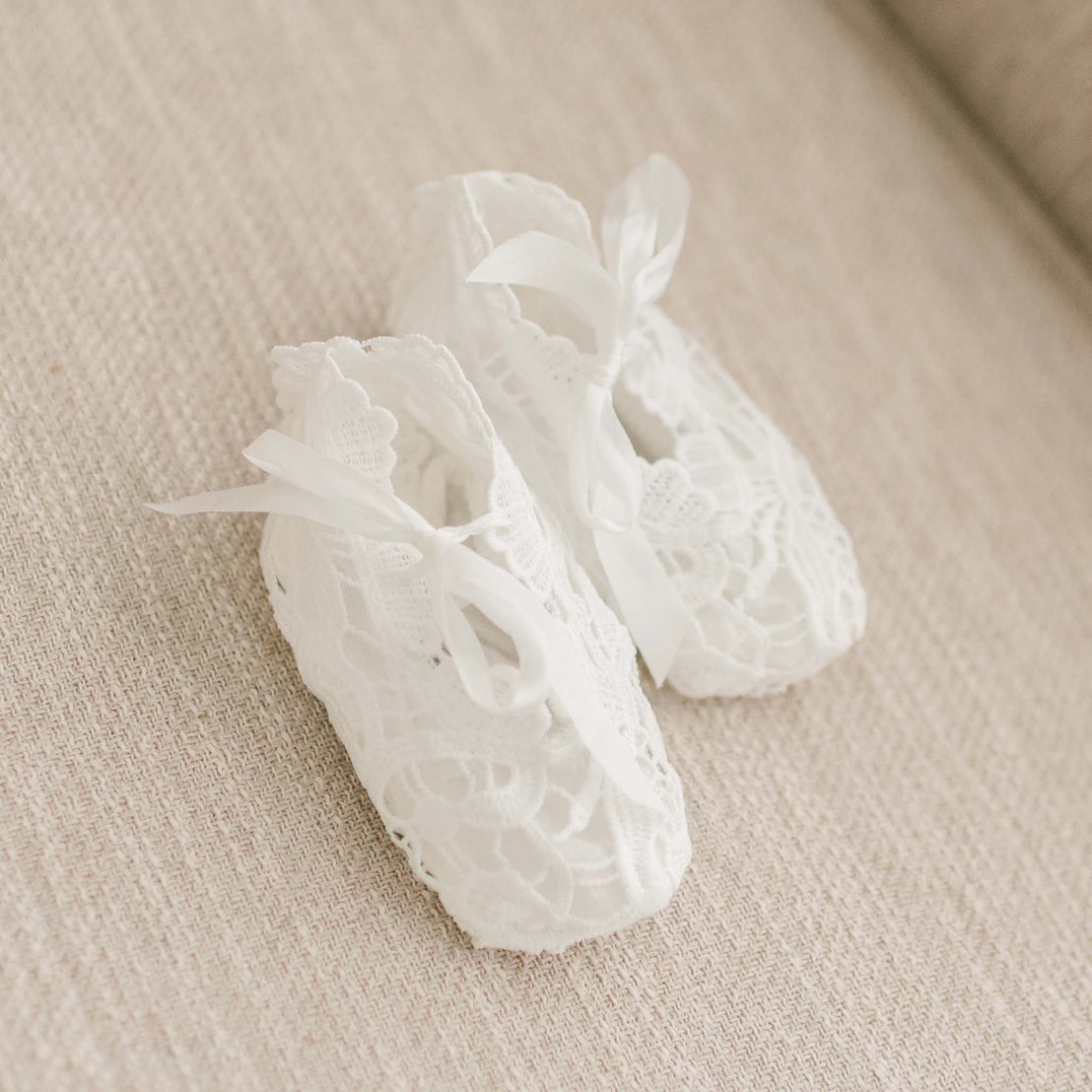 Flat lay of the Lola Booties made with an all-over lace in a light ivory color and a silk bow tie.