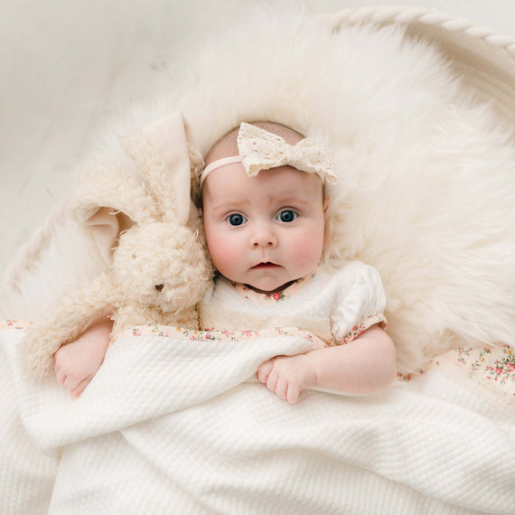 Newborn baby girl underneath a blanket holding the Eloise Bunny, a super soft stuffed animal with a tan scraggly fur body.