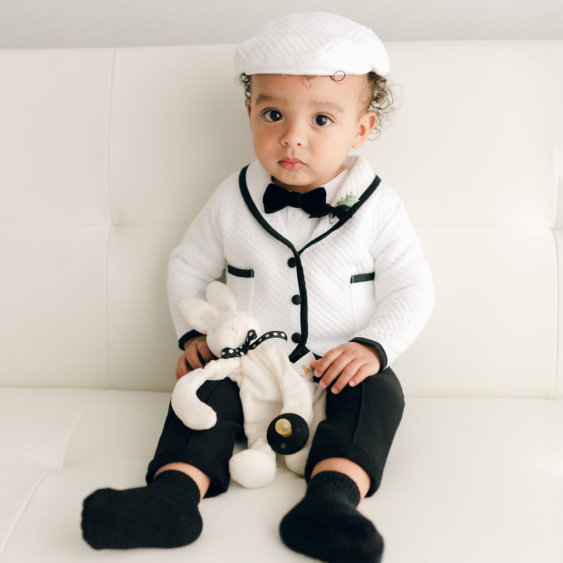 Baby boy sitting on a couch and wearing the white James 3-Piece Suit (and matching Newsboy Cap).