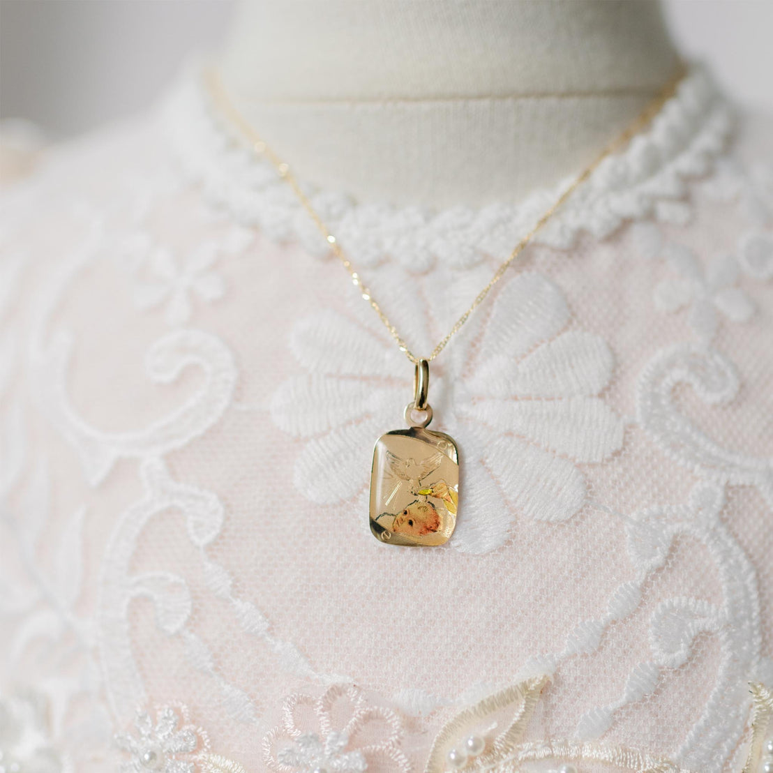Gold necklace with a pendant on a mannequin wearing a white lace garment.