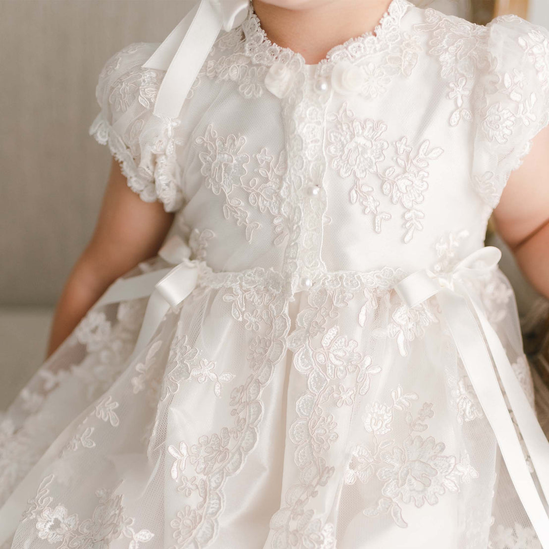Close up photo of floral lace details on the Penelope full-length christening gown, part of the Baby Beau & Belle baptism collection.