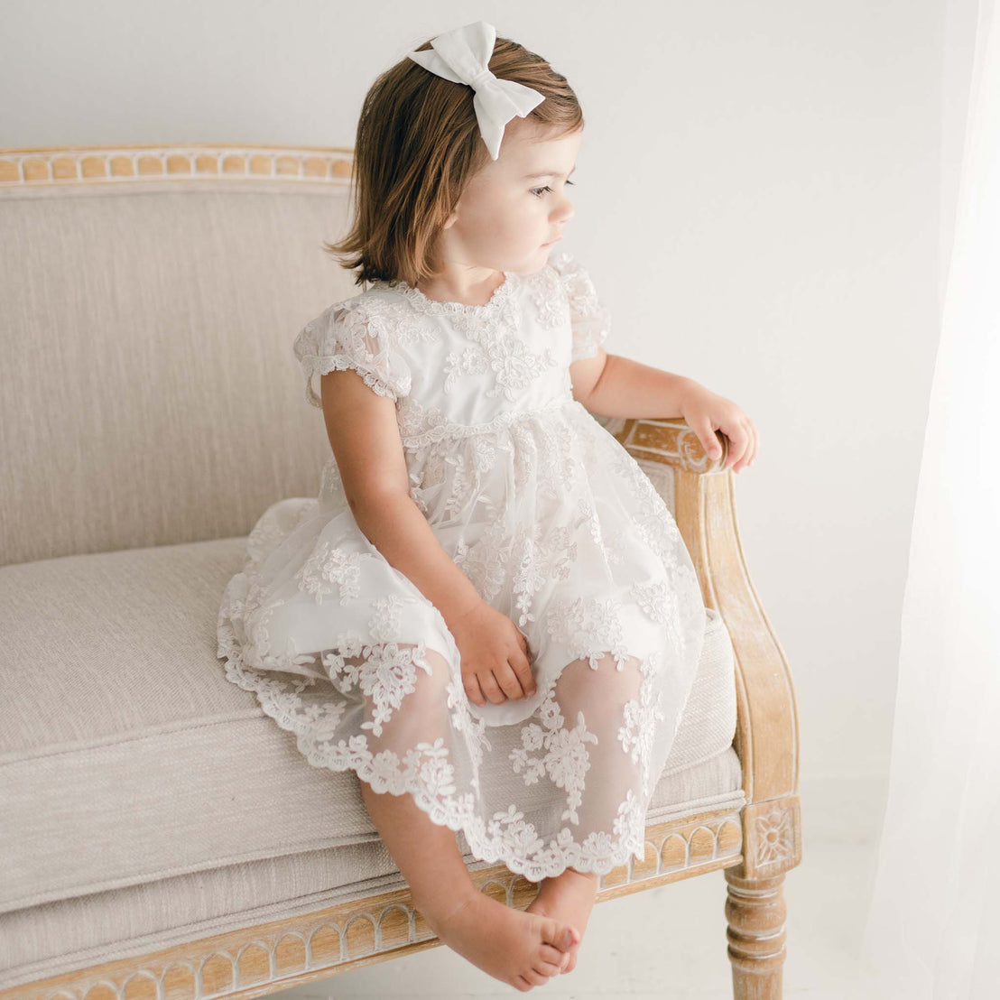 Baby girl sitting on chair wearing her beautiful lace christening dress. 