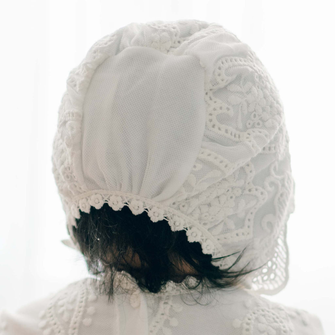 A close-up of the back of a Eliza Bonnet as featured on a baby girl with dark hair. The close-up highlights the detailed lacework on the Eliza Bonnet.