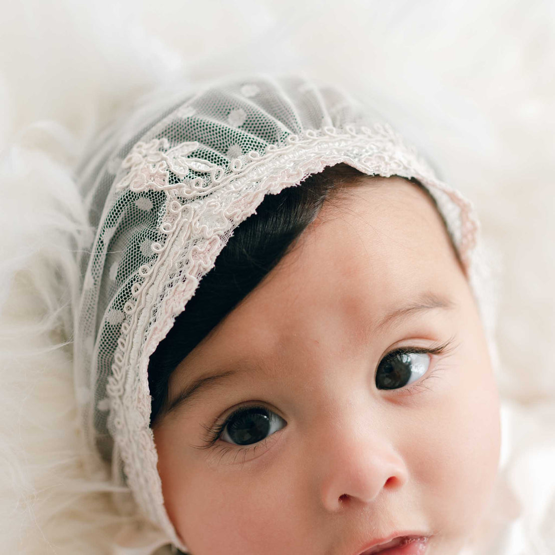 Close-up of a baby in the Elizabeth Newborn Christening Bonnet, featuring the ivory and pink edge laces along the front of the sheer bonnet.