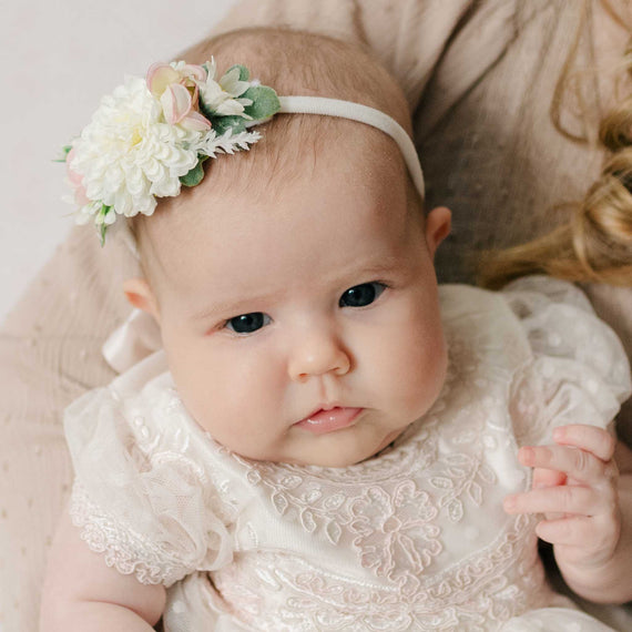 Newborn baby wearing the Elizabeth Flower Headband and matching dress. The floral headband features pink and cream flowers with greenery along a nylon headband, perfect for unique baby gifts.