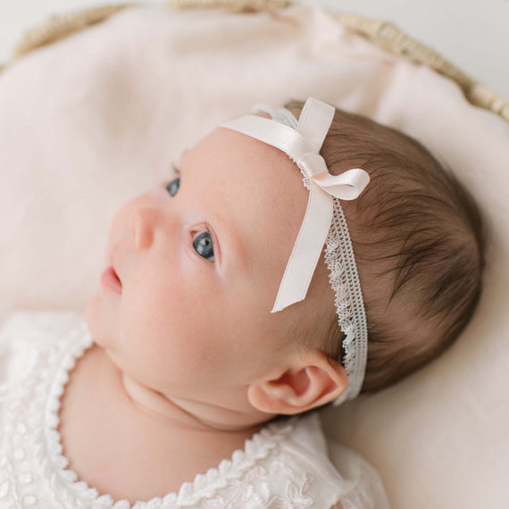 Newborn baby wearing an Elizabeth Silk Ribbon Headband with a pink silk ribbon bow, lying on a soft surface.
