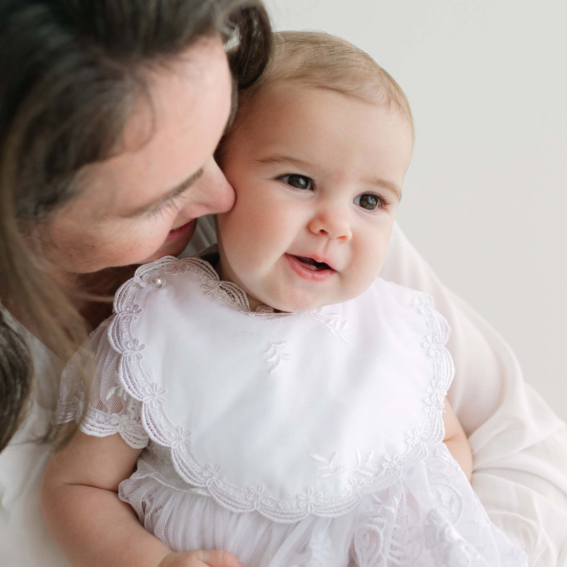 Woman holding a baby in a white dress with a lace bib.