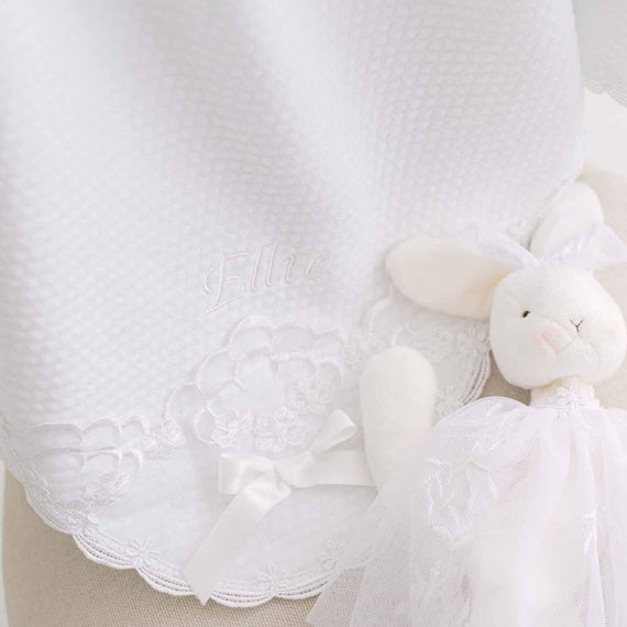 White quilt blanket with the name "Ellie" embroidered on the corner and a plush rabbit toy on a neutral background.