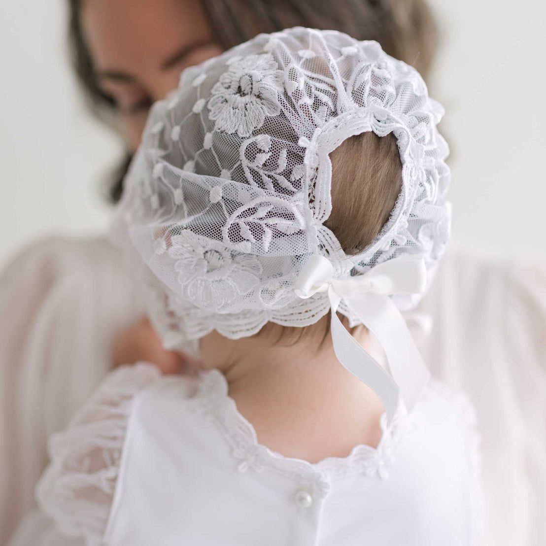 Baby wearing a white lace bonnet with a blurred background.