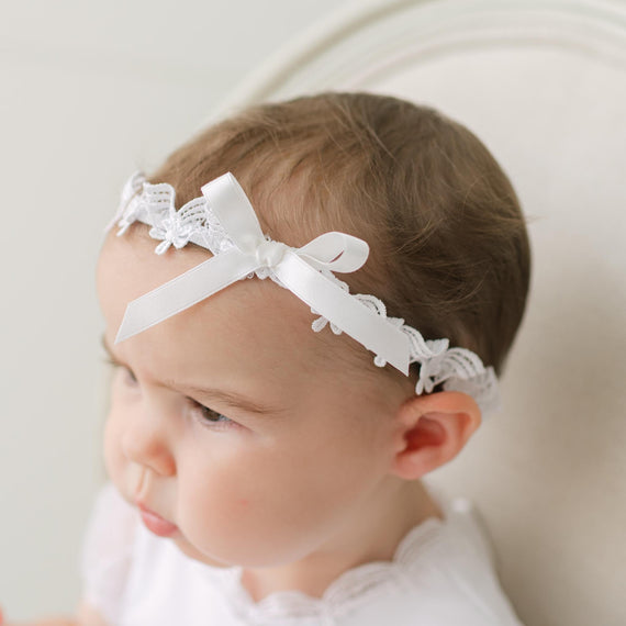 Baby wearing a white lace headband with a neutral background.
