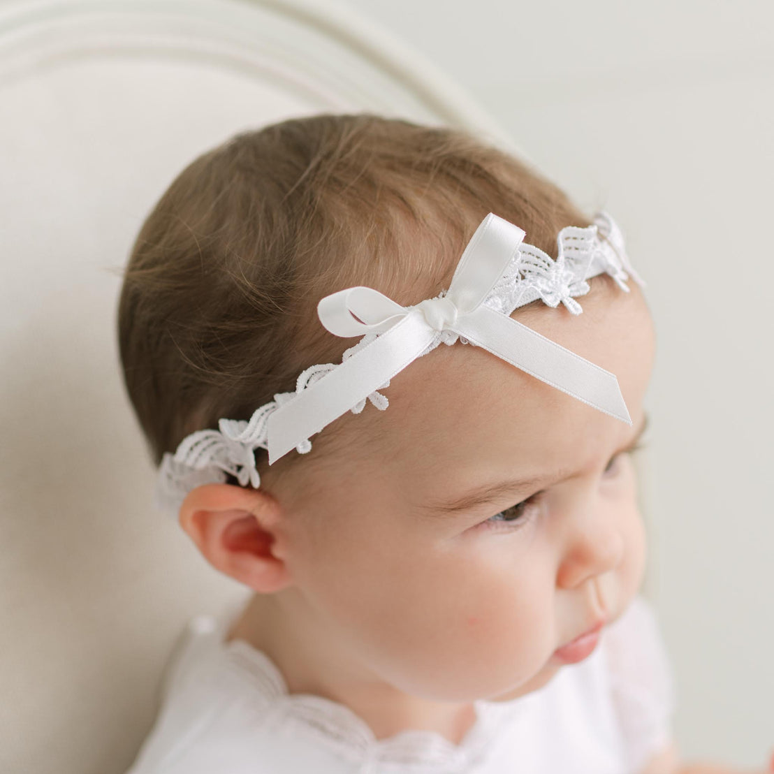 Baby wearing a white lace headband with a neutral background.