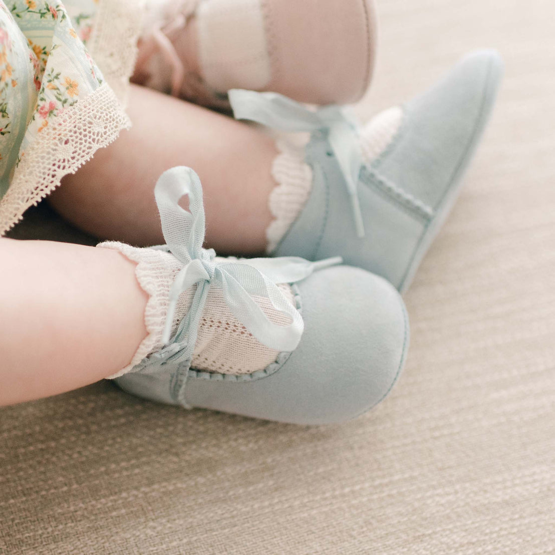 Baby girl wearing the "sky blue" color Eloise Suede Tie Mary Janes. These shoes are made with super soft suede with tie detail closures. 