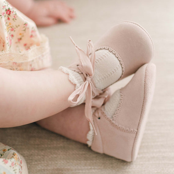 Baby girl wearing the "blush" color Eloise Suede Tie Mary Janes. These shoes are made with super soft suede with tie detail closures. 