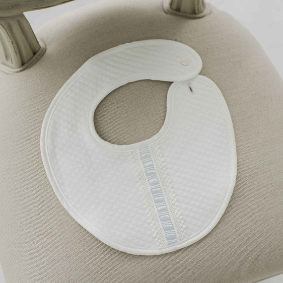 A white quilt bib with blue silk ribbon on a beige background.