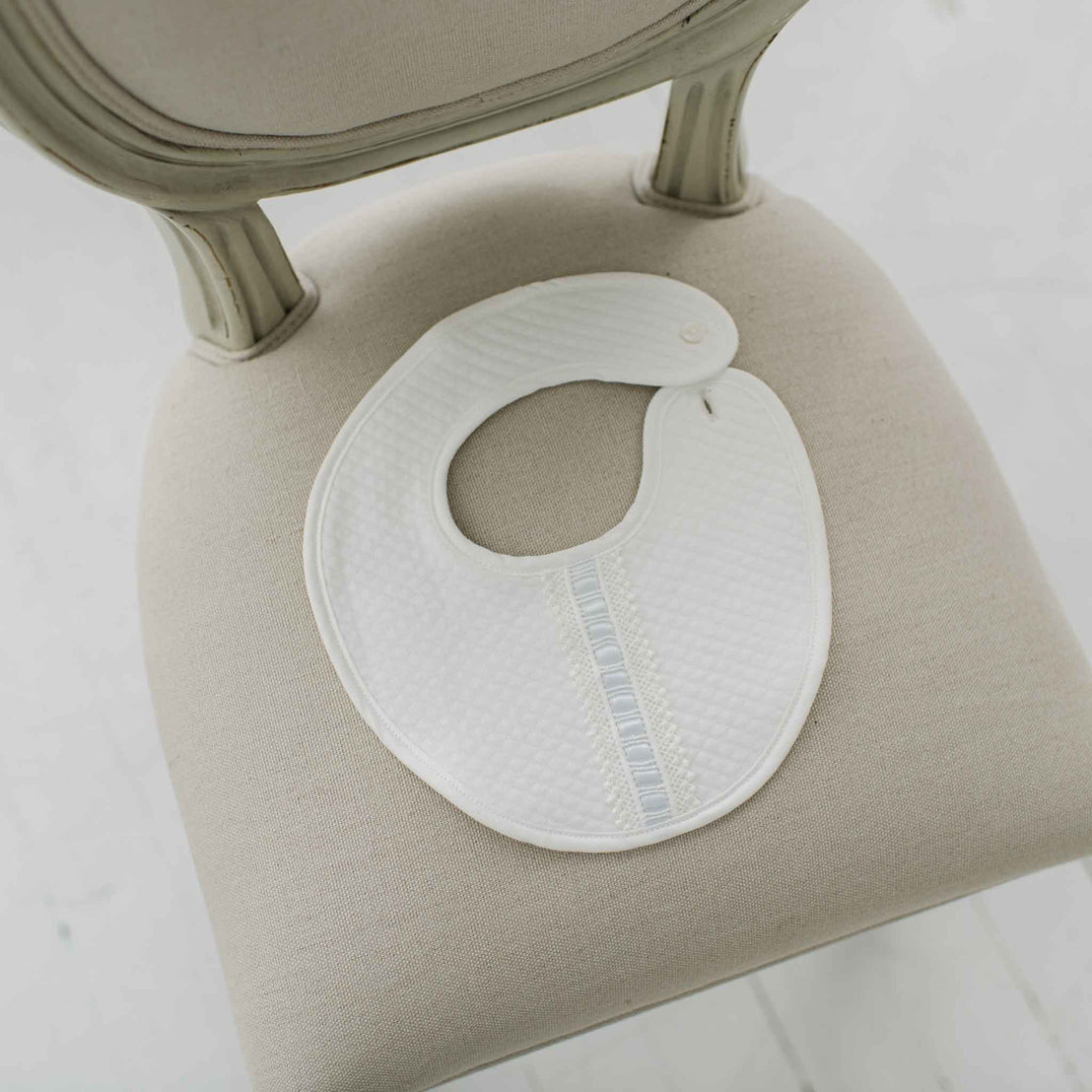 White bib with blue silk ribbon on a beige chair.