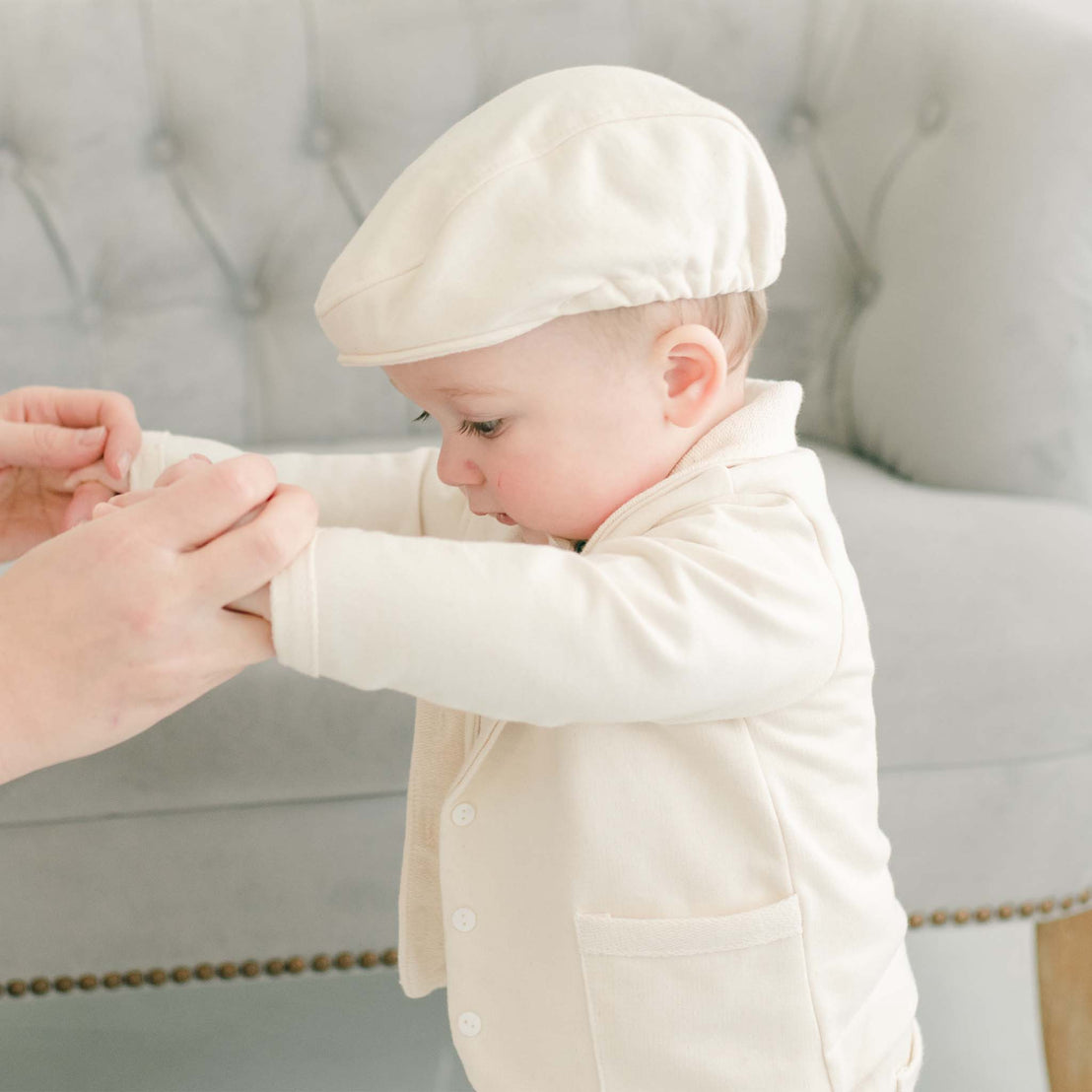 Closer detail of baby boy being guided by his mother. He is wearing the Ezra Tan 4-Piece Suit with matching newsboy cap