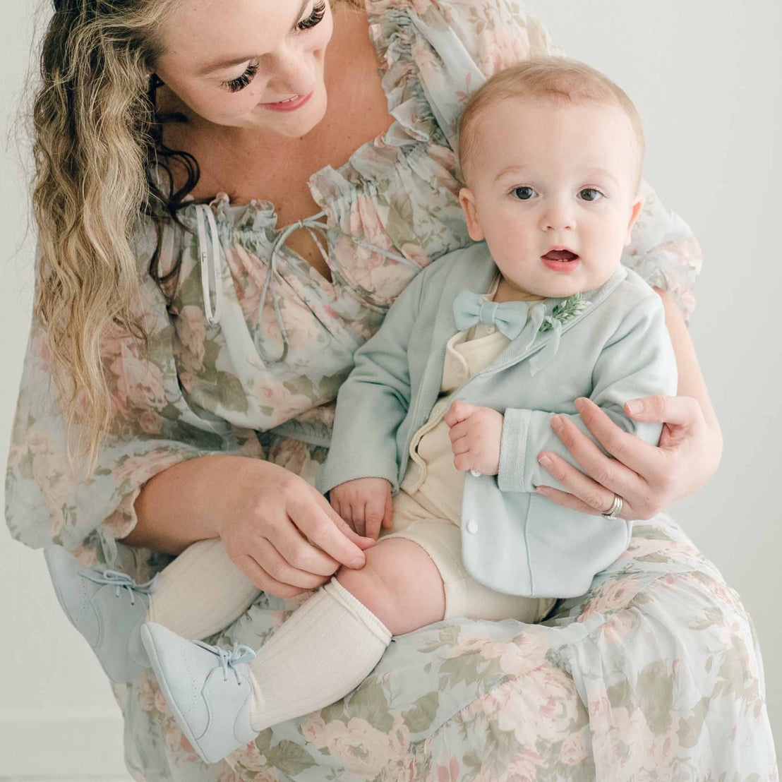 Baby boy sitting on his mother's lap. He is wearing the Ezra 4-Piece Powder Blue Suit, blue velvet bow tie and boutonniere