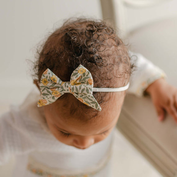 Top view of a baby wearing the Petite Fleur Bow Headband, featuring a floral cotton bow on a soft, stretchy nylon band.