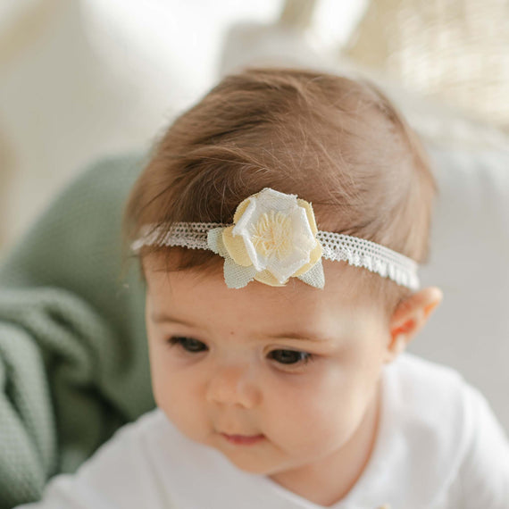 Close-up of a baby wearing the Petite Fleur Linen Flower Headband, featuring a soft stretch lace band and a delicate linen flower accent in light yellow and ivory.