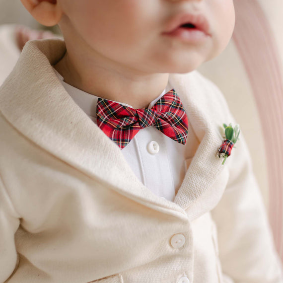 Outfitted in a cream cardigan and white shirt, the baby showcases the Gabriel Bow Tie & Boutonniere set, featuring a striking red plaid bow tie paired with a small green boutonniere. This delightful ensemble is perfect for the holidays, offering meticulous detail to add a festive touch.