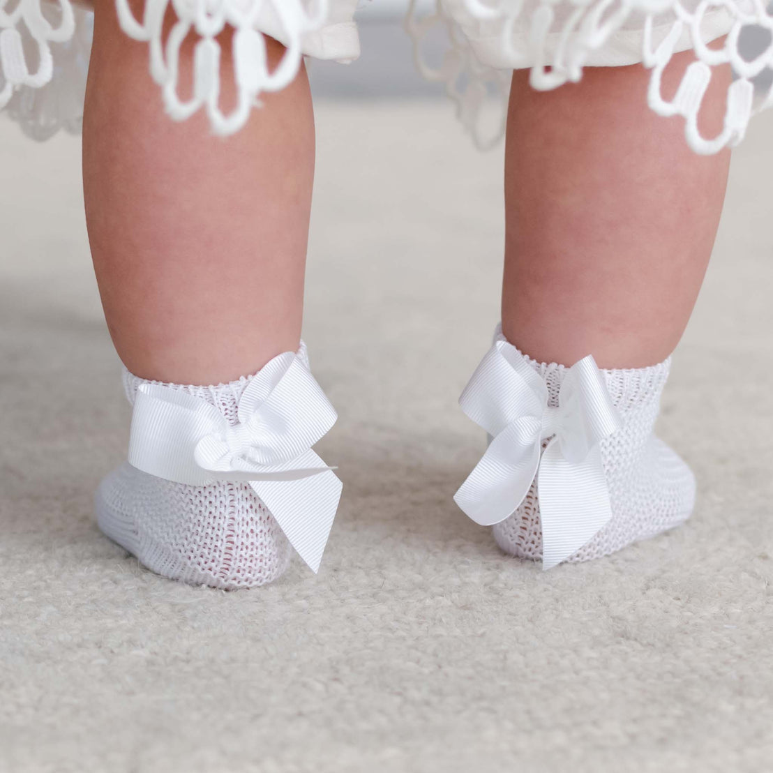 Close-up from behind of a baby's feet in the Garter Stitch Socks with Bow. The socks are knitted with a grosgrain ribbon detail.