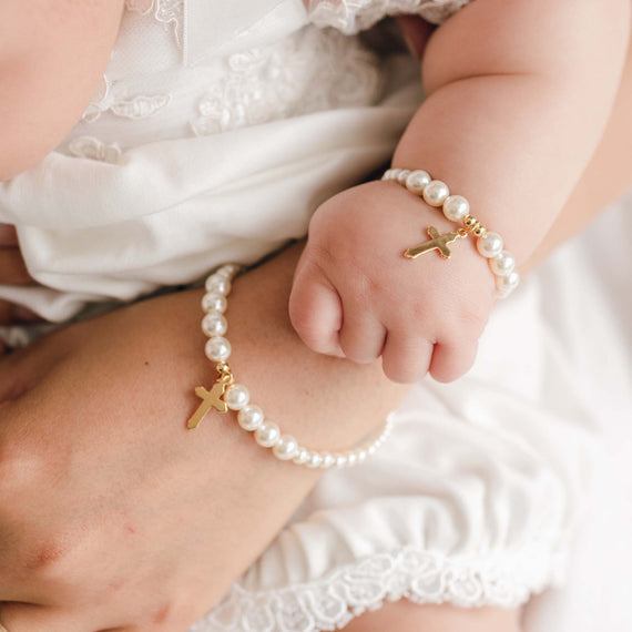 Close-up of a hand and child's hand holding together, both wearing pearl bracelets with gold crosses.