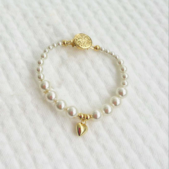 Cream pearl baby bracelet with gold plated heart charm on a white textured background
