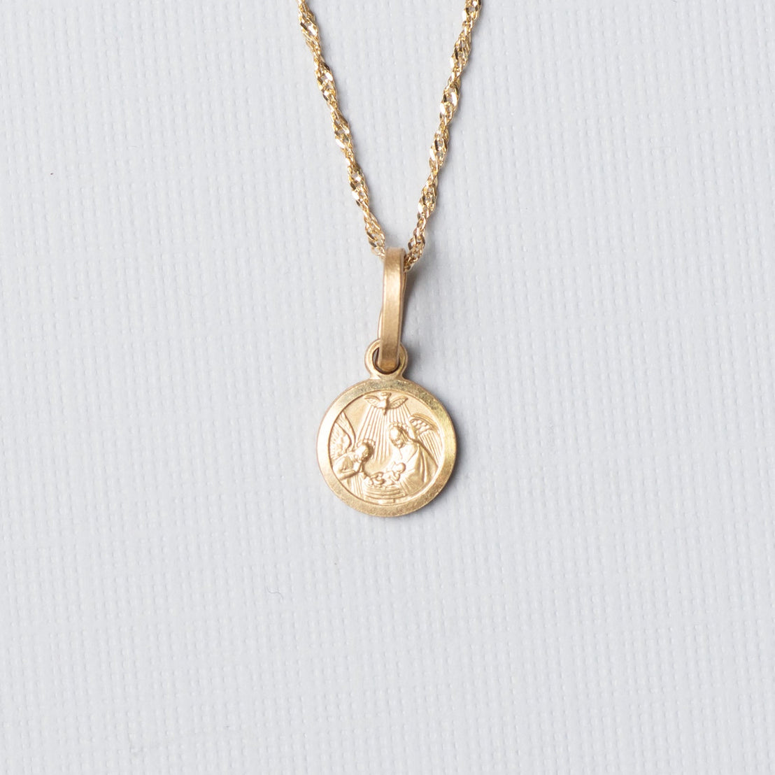Gold necklace with a round pendant on a light gray background