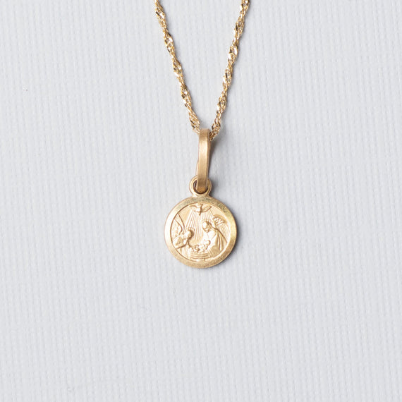 Gold necklace with a round pendant on a light gray background