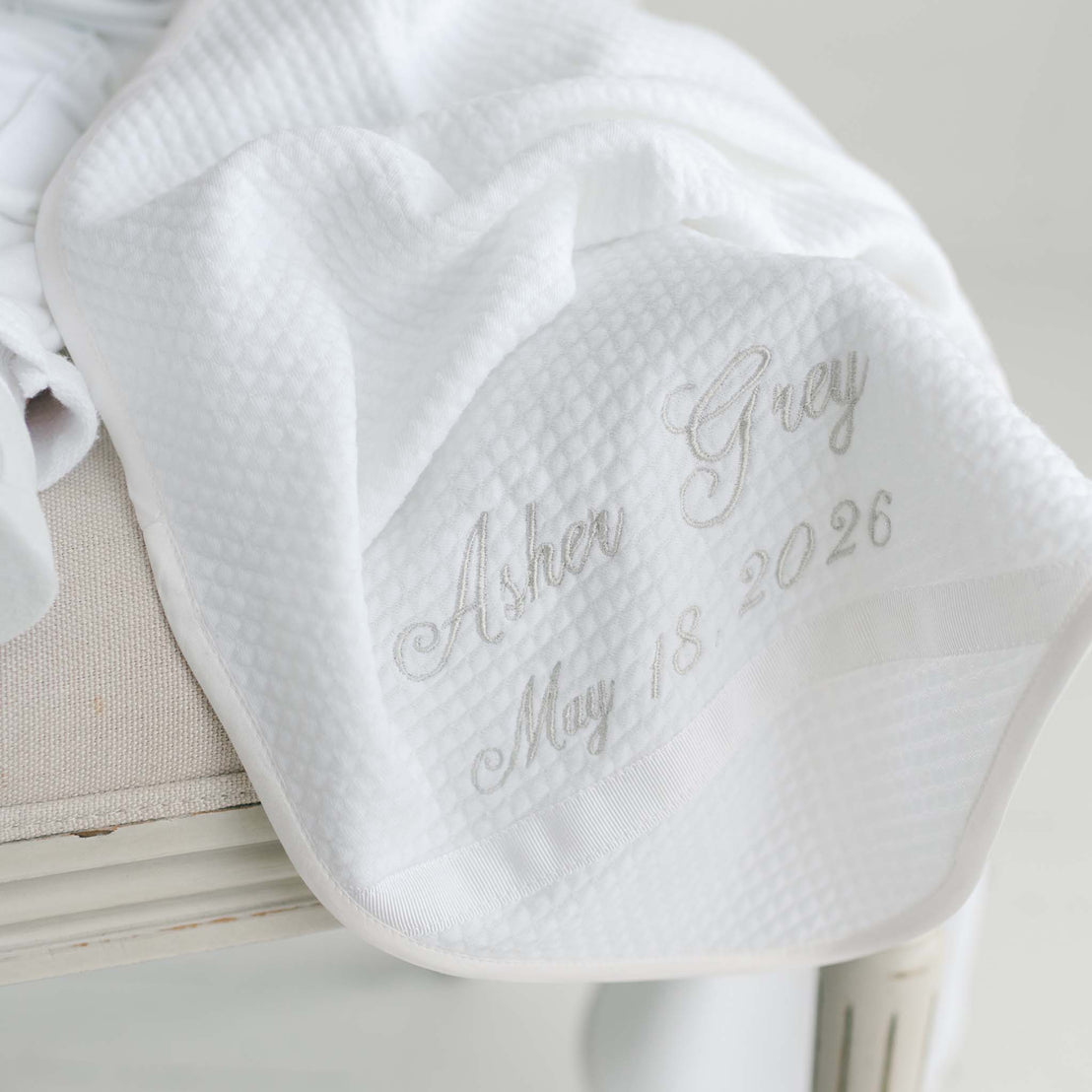 White baby blanket with embroidered text on a light background.