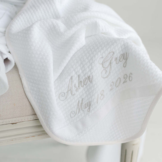 White baby booties with embroidered text on a light wooden surface