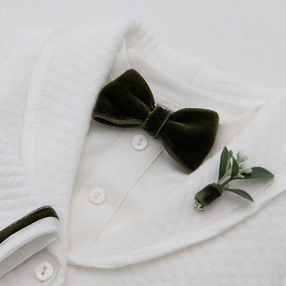 A close-up of a Noah Green Bow Tie & Boutonniere on an upscale white dress shirt collar, adorned with a small green plant pin and a vintage heirloom texture.