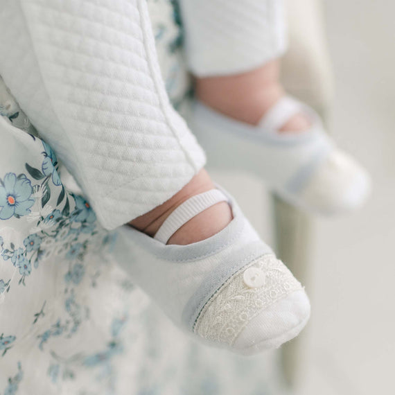 Close-up of a baby's feet wearing soft, quilted Harrison Booties, accented with lace detailing and a small button, paired with matching quilted pants.