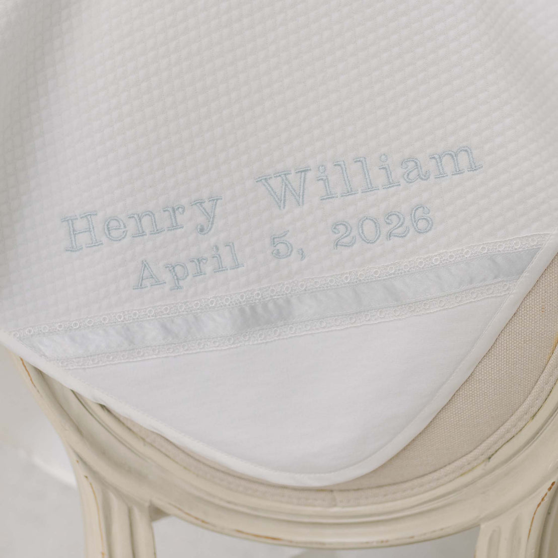 Close up photo of the Henry Personalized Blanket draped on a beige chair. Perfect as a baptism gift from godparents.