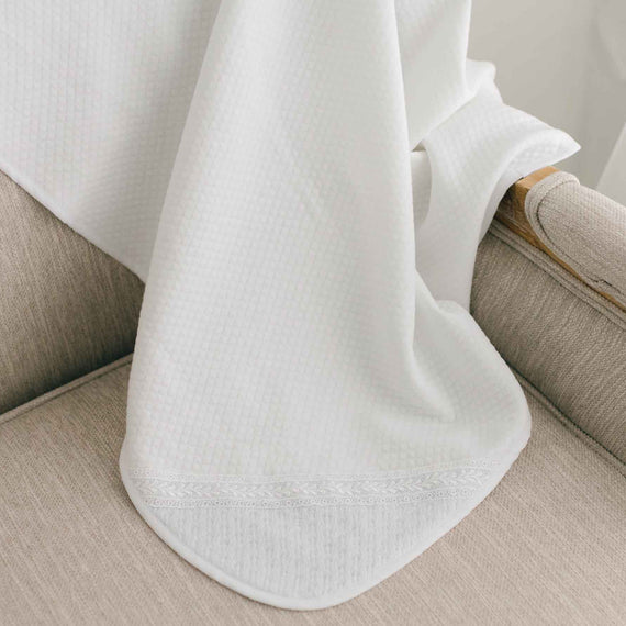 White blanket with embroidered corner draped over a chair.