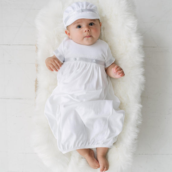 Baby in a white outfit and hat lying on a white rug